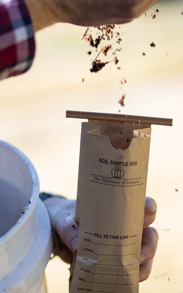 Person taking a soil sample in a brown soil sample bag