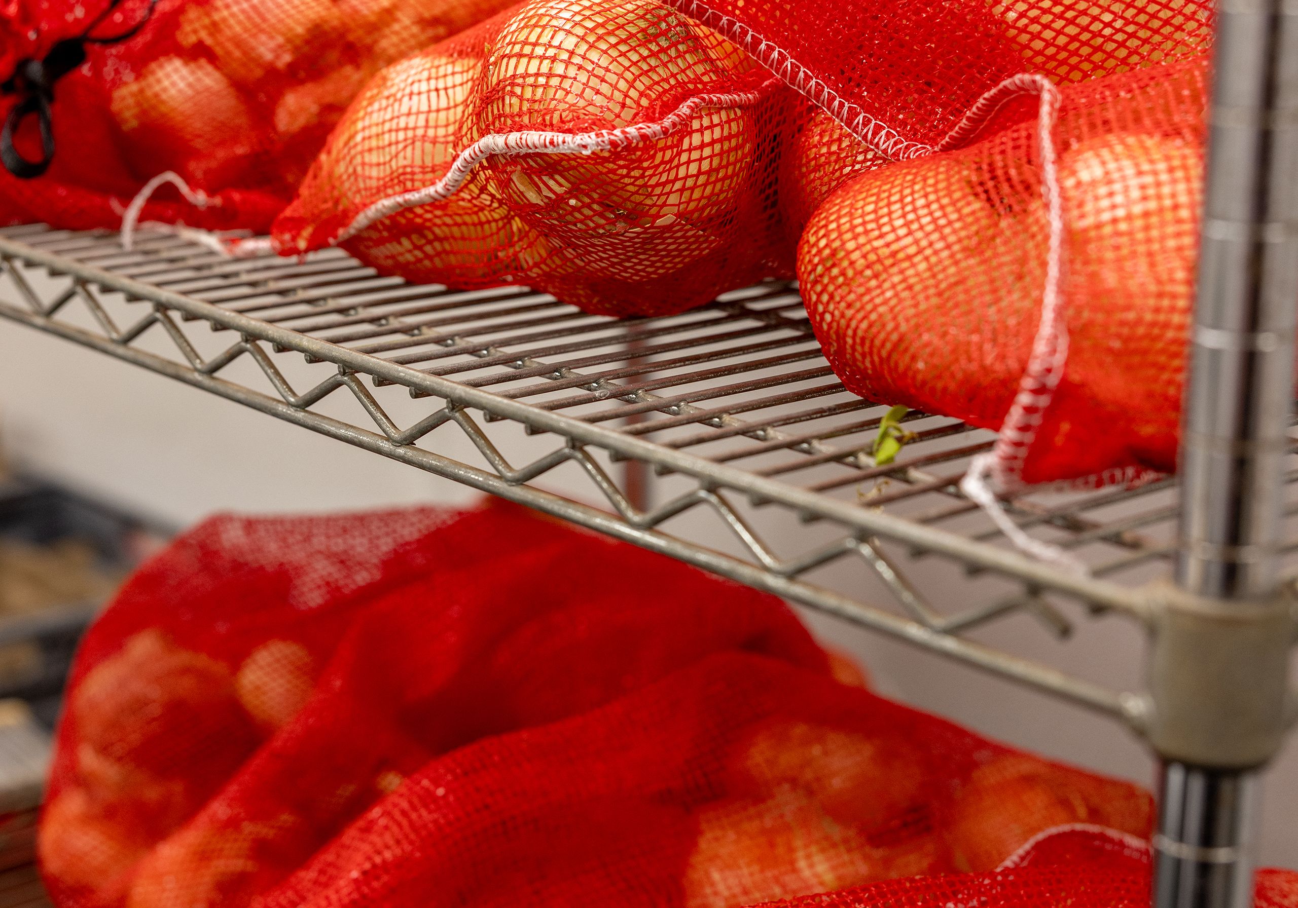 Red bags of onions await testing on a steel shelf.
