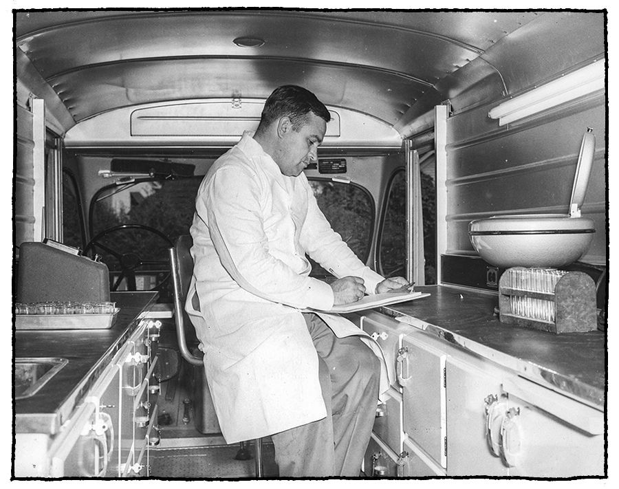 1950s era black and white photo of a man in a lab coat inside a soil testing truck