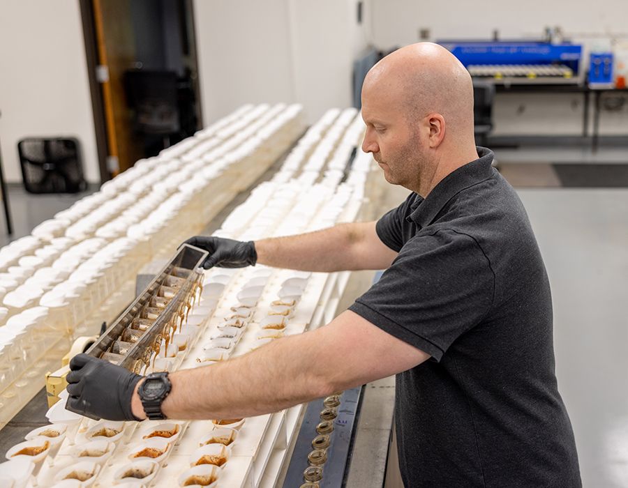 A man in gloves pours soil slurry from a rack into funnels for nutrient analysis in a lab.