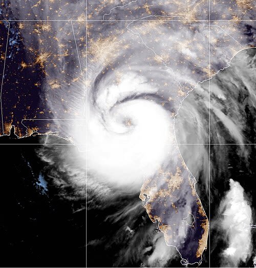 Satellite image of a large hurricane with a defined eye, swirling clouds, and storm system over the southeastern United States coastline.