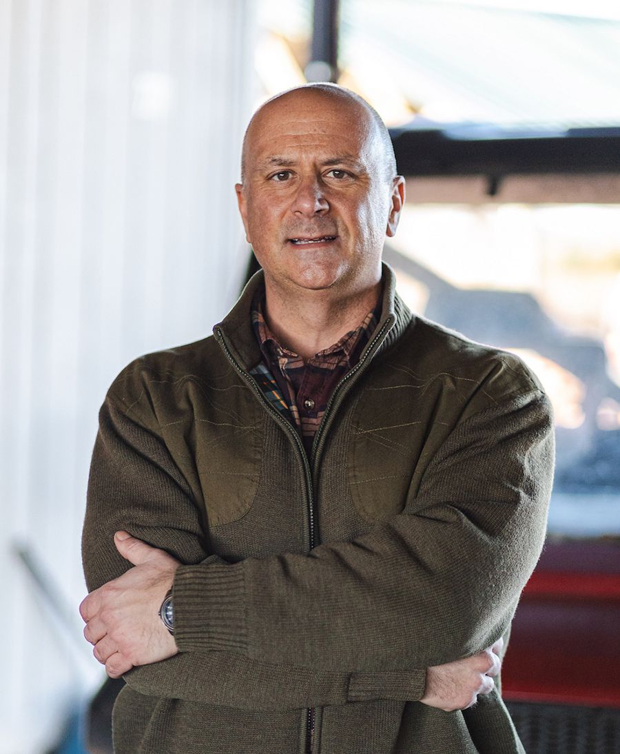 Man standing with arms crossed, wearing a green zip-up sweater over a plaid shirt.
