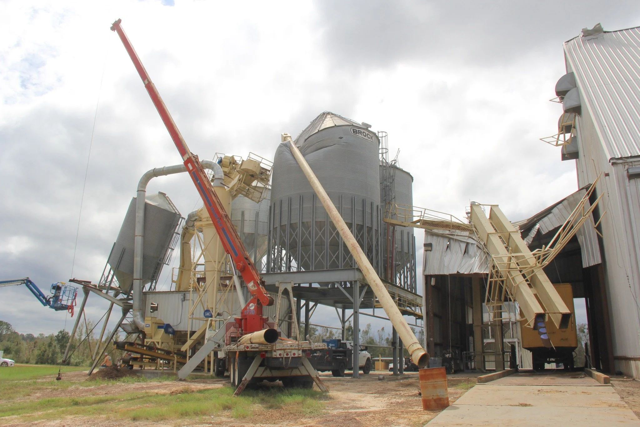 Damaged agricultural processing facility with collapsed structures, tilted silos, and broken conveyors after a storm.