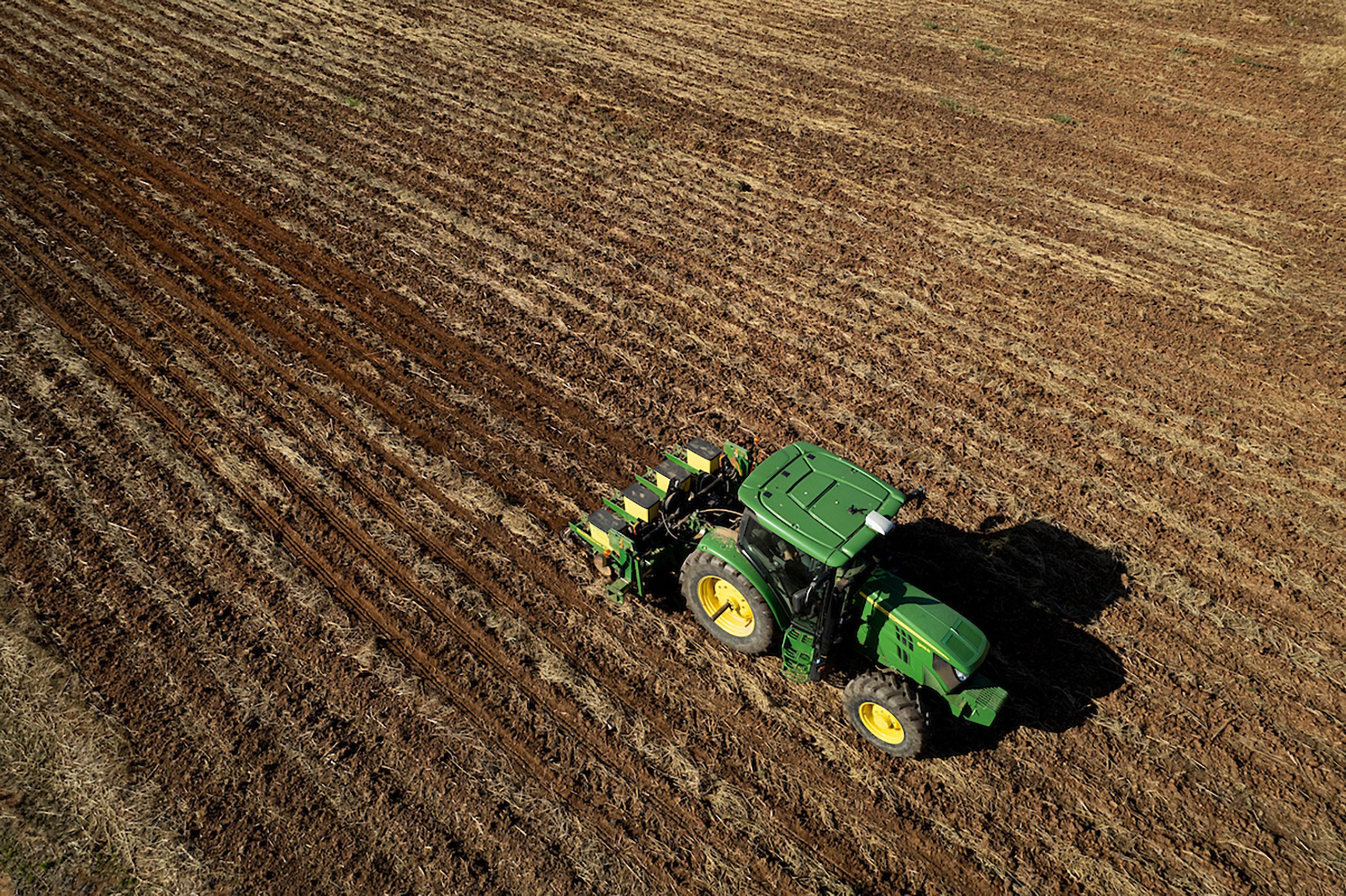 A green tractor travels down brown field rows.