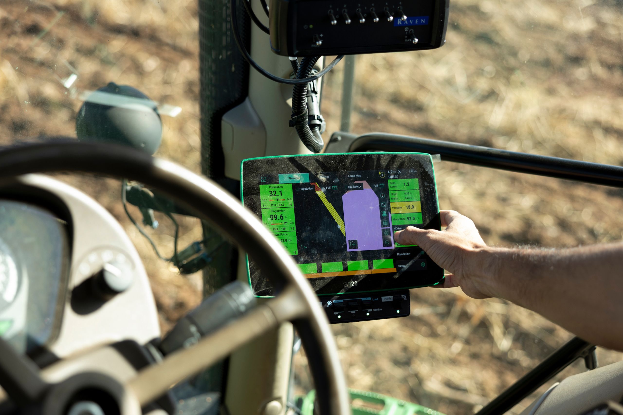 A farmer in the cab of a tractor looks at the screen of a gps monitor. 