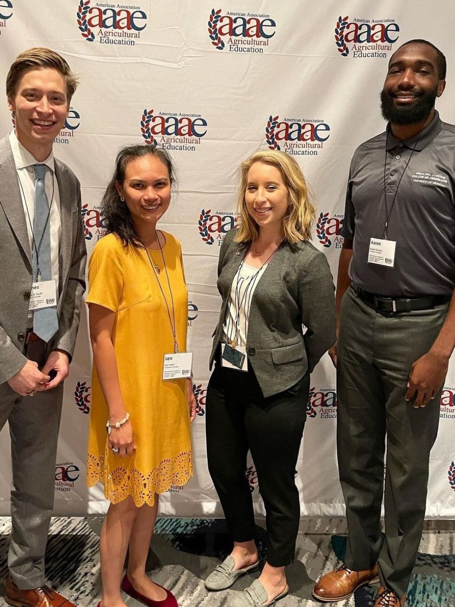 Four ALEC students (one white man, two white women, one Black man) in front of a step and repeat for the American Association of Agricultural Education.