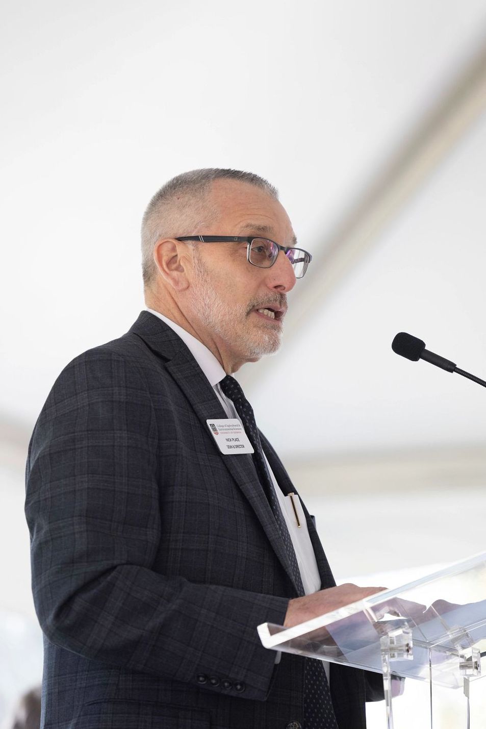 Dean Nick Place speaking at a podium under a white tent.