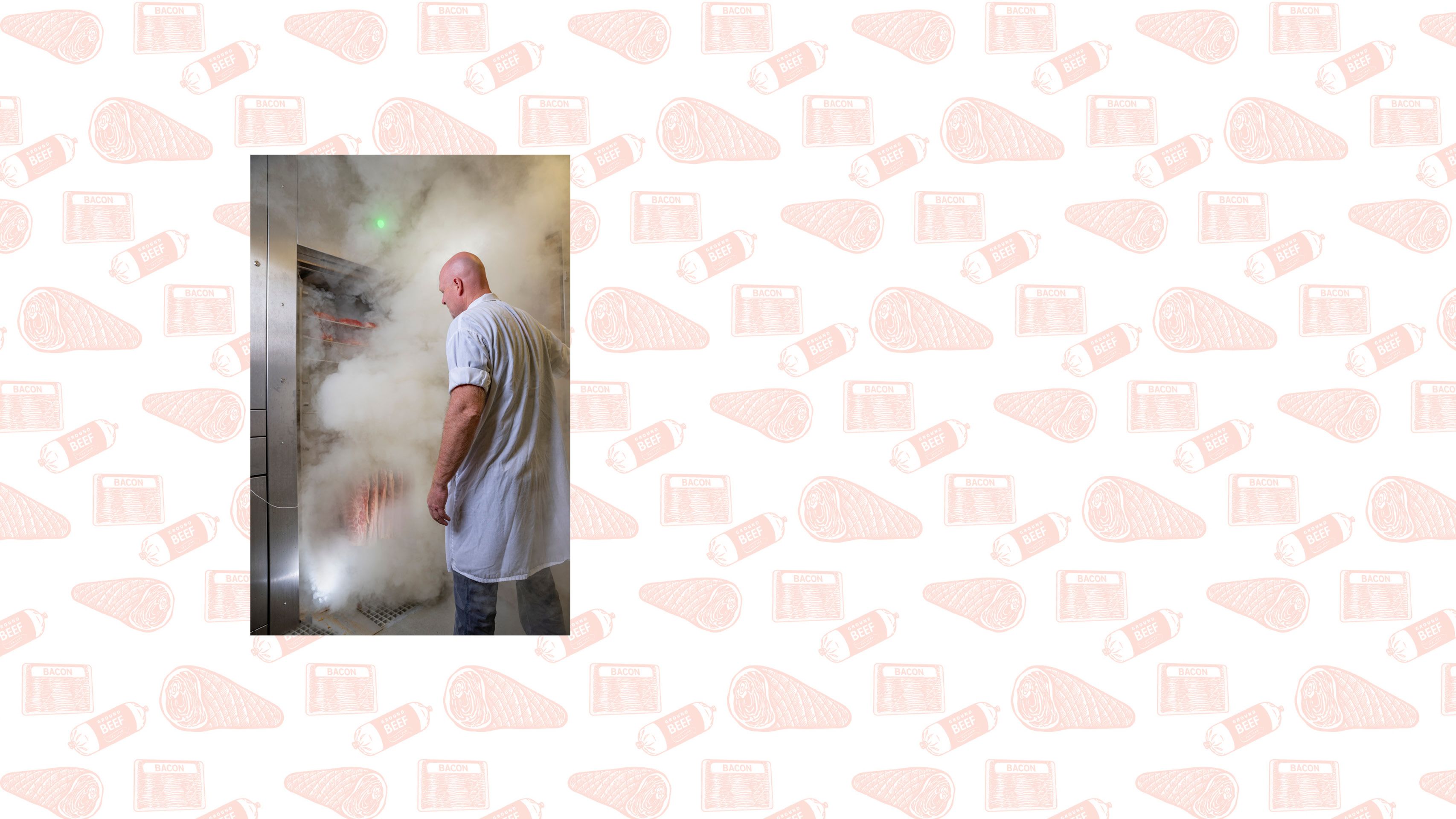 A white man in a white coat opens the door to a meat smoker. Lots of white smoke is billowing out of the smoker.