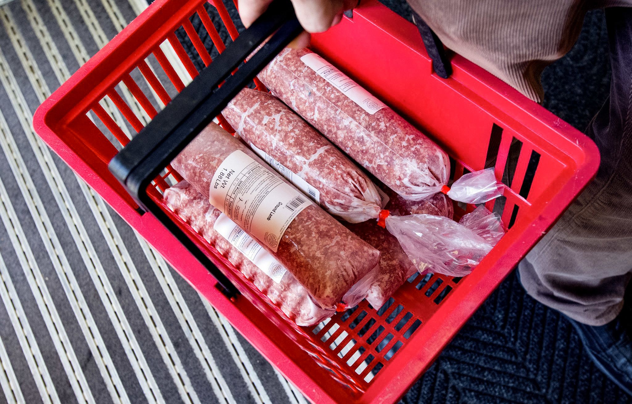 Packages of ground meat inside a red shopping basket.