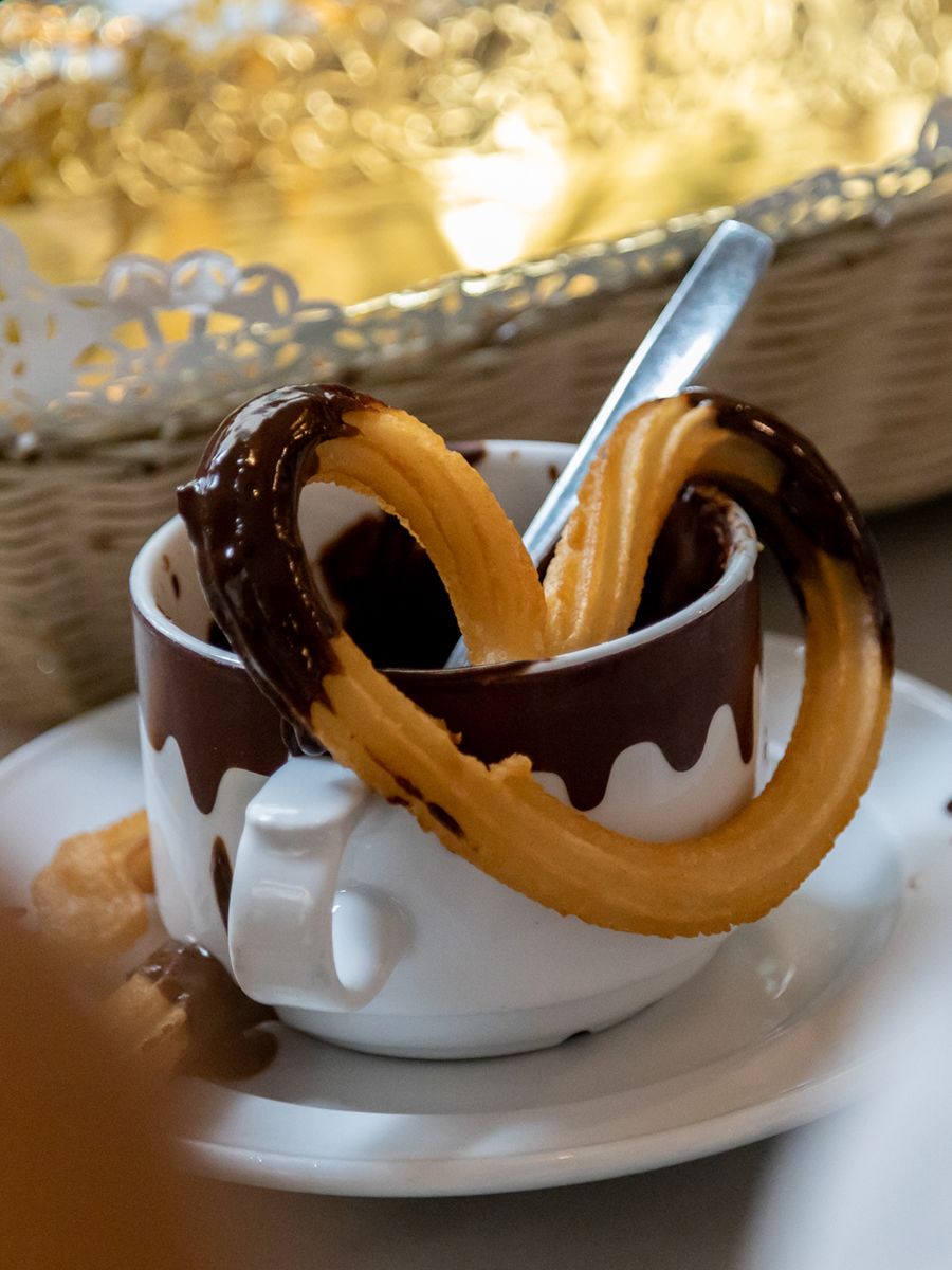 A pretzel-shaped churro rests on a mug of melted chocolate.