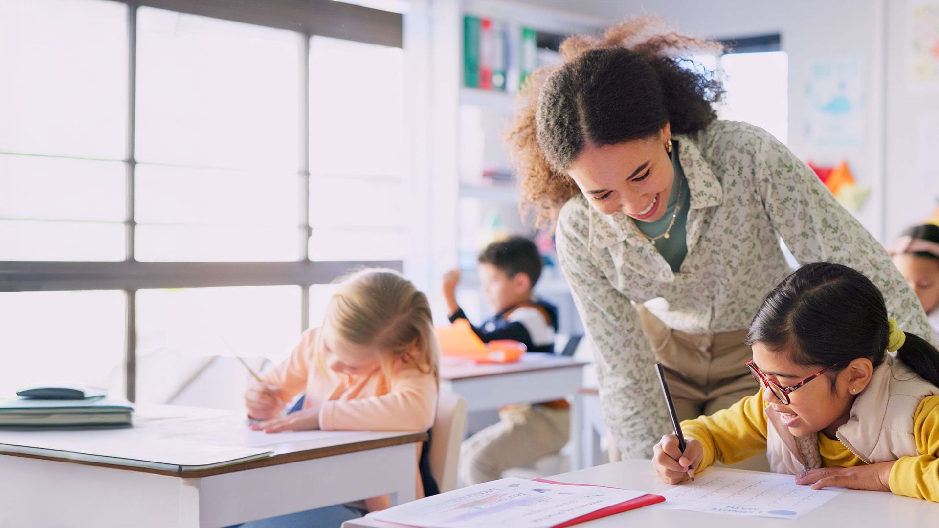 A teacher working with a student in a classroom setting. Both are smiling.