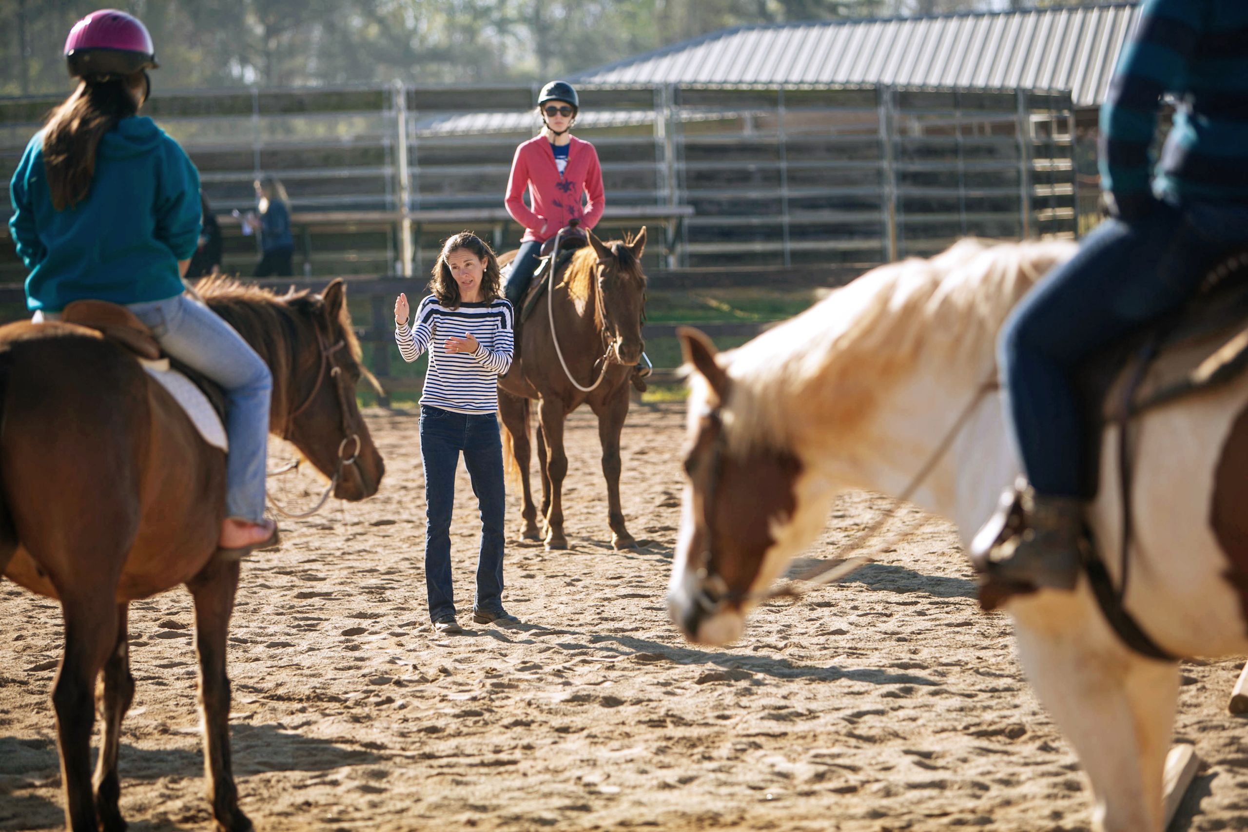 Associate Professor Kylee Jo Duberstein stands in a paddock surrounded by students on horseback.