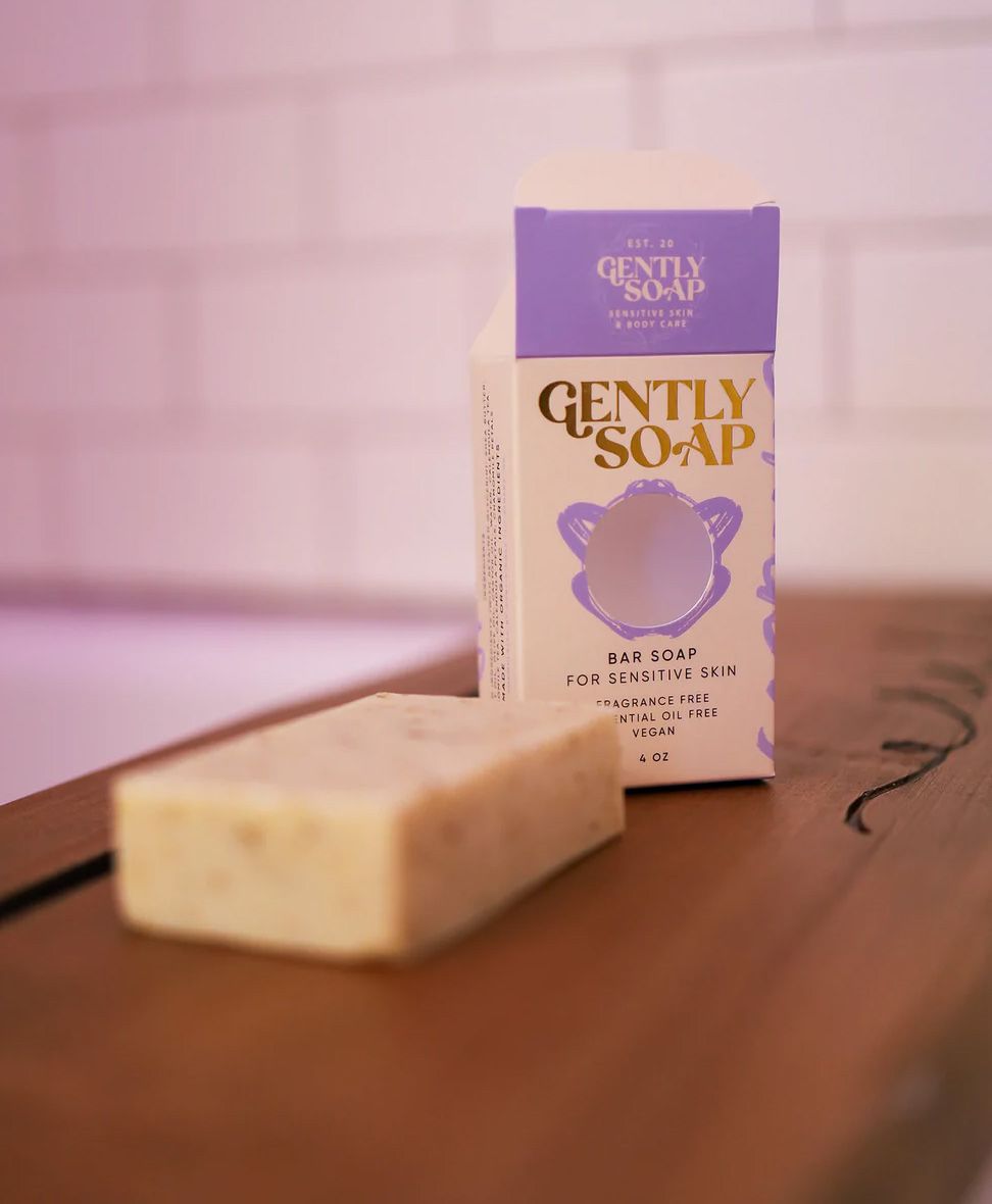 A bar of Gently brand soap sits on a board in a tile bathroom